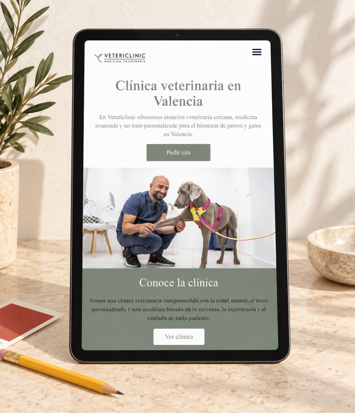 web de Vetericlinic en una tablet, con un veterinario atendiendo a un perro.